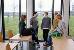 Ein Gruppenfoto von Studierenden im Seminarraum mit dem TU Dortmund Logo. Sie sprechen miteinander und schauen sich an.